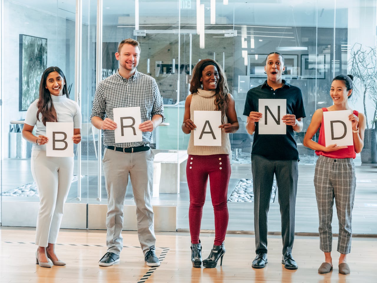 Diverse business team smiling and holding signs spelling 'BRAND' in a modern office.